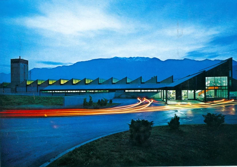Die neue PLANK-Fabrik in der Abenddämmerung, Licht in den Sheddächern, dahinter die Berge
